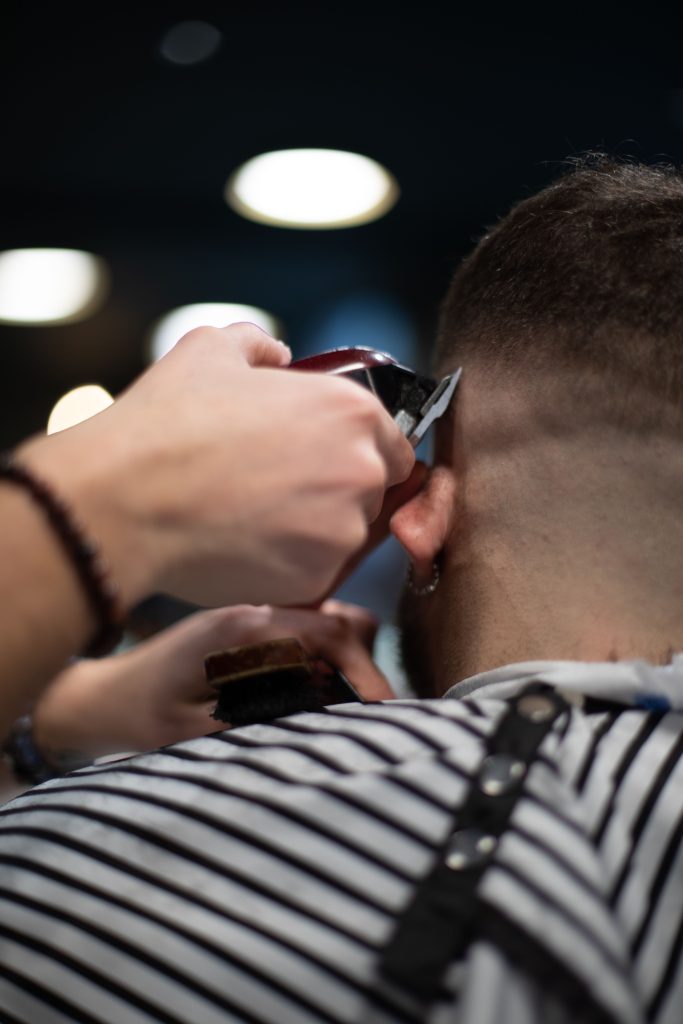 Kapper werkt de nek van een klant bij met een tondeuse, met beide handen bezig en dus niet vrij om de telefoon op te nemen